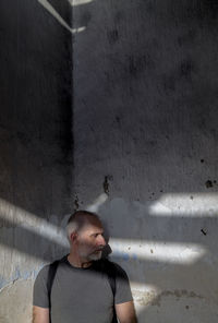 Portrait of adult man looking away while standing on old wall with sunlight and shadow