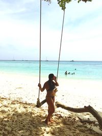 Rear view of shirtless boy on beach against sky