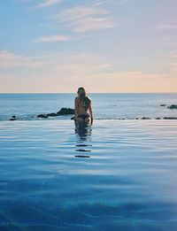 Rear view of woman swimming in infinity pool against sky during sunset