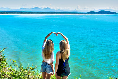 Rear view of women gesturing against sea