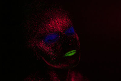 Close-up of woman with glowing face paint against black background