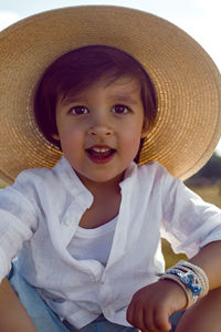 Baby boy in straw hat and blue pants sitting on a haystack in a field in autumn