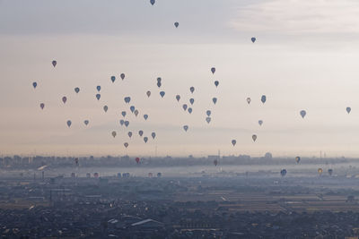 Flock of hot air balloons flying in city against sky