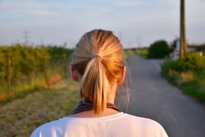 Rear view of woman with ponytail standing on road against sky