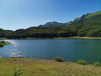 Scenic view of lake and mountains against clear blue sky