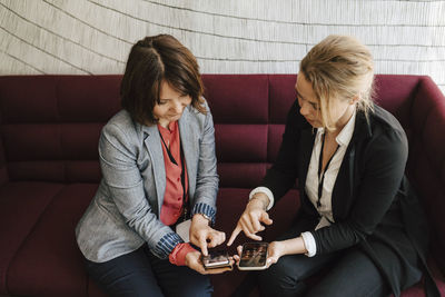 Businesswomen discussing over smart phones while sitting on sofa at convention center