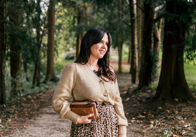 Smiling young woman standing by tree trunk in forest