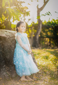 Full length of cute girl wearing dress standing by rock in park