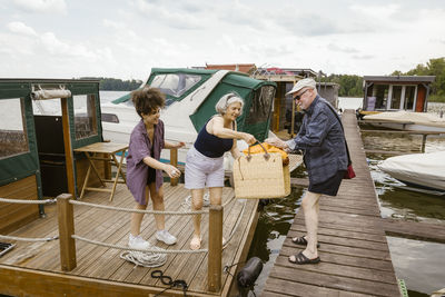 Full length of man giving basket to woman on houseboat against sky