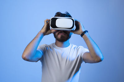 Young man using virtual reality simulator against blue background
