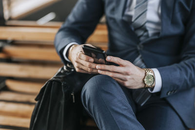 Midsection of businessman using smart phone while sitting on bench