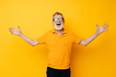 Senior man gesturing against yellow background