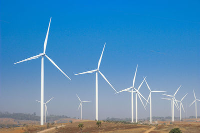 Windmills on field against clear blue sky