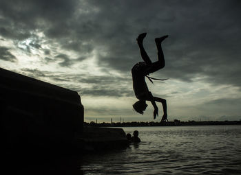 Silhouette man jumping in water against sky