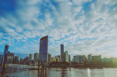 City by river and buildings against sky