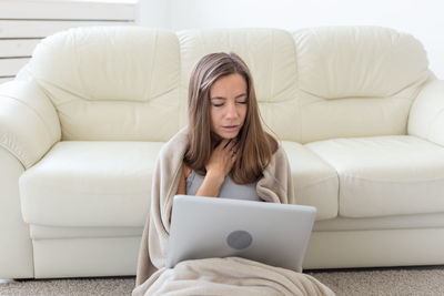 Young woman using phone while sitting on sofa at home