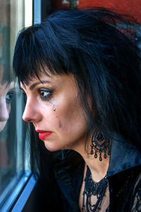 Close-up of woman crying against window at home