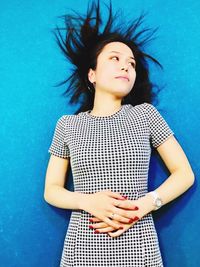 Young woman looking away while standing against blue wall