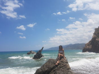 Woman sitting on rock by sea against sky