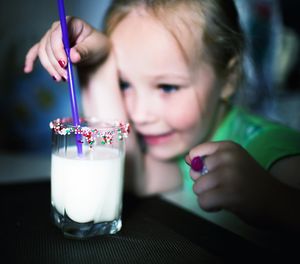 Playful girl holding drinking straw in glass of milk