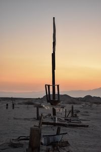 Wooden posts on beach against sky during sunset