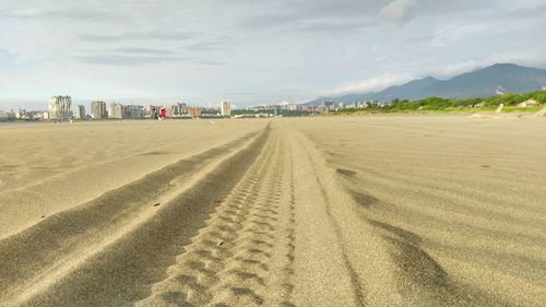 Tire tracks on beach against sky