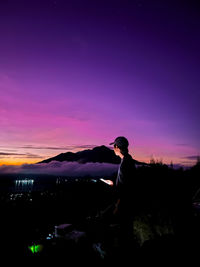 Rear view of man sitting on rock against sky during sunset