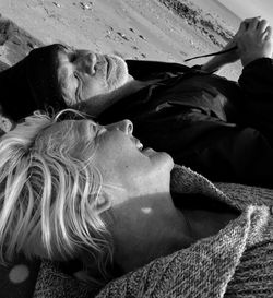 Close-up of smiling woman and man lying on sand at beach