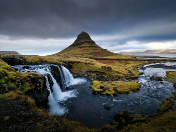 Waterfall with cloudy sky and green grass in iceland. kirkjufell.
