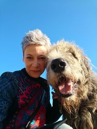 Portrait of smiling woman with dog against blue sky