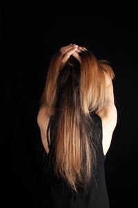 Rear view of woman with hands in hair standing against black background