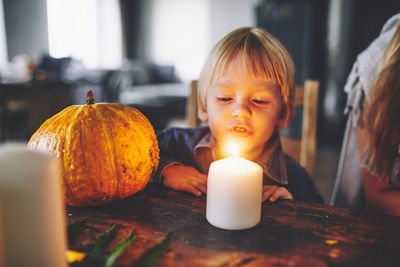 Close-up of boy sitting by candle on table