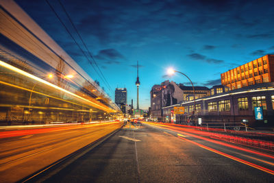 Light trails on road amidst buildings at dusk