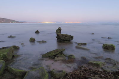 Rocks on sea shore against sky during sunset