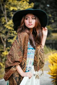 Portrait of beautiful young woman standing against tree