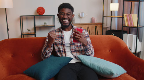 Young woman using phone while sitting on sofa at home