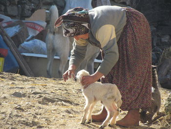 Woman feeding kid goat with milk at farm