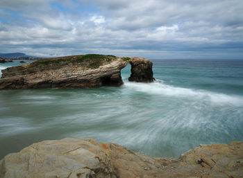 Rock formations in sea against cloudy sky