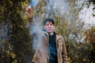 Portrait of young man holding distress flare while standing in forest