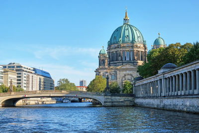 Arch bridge over river amidst buildings against sky in city