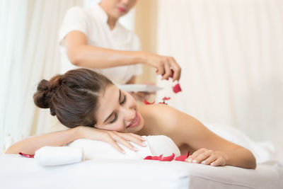 Masseur putting flower petals on young woman in spa