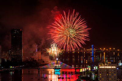 Firework display over illuminated buildings and river in city at night