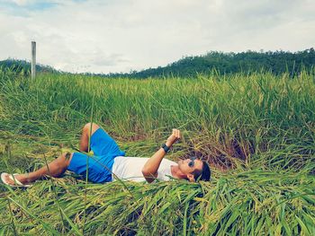 Woman lying on grass against sky