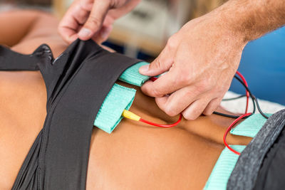 Midsection of physical therapist using electrical stimulation on womans back for treatment