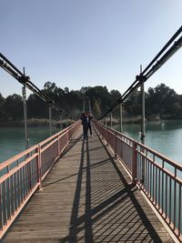 Rear view of man on footbridge over river against sky