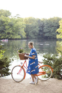 Man riding bicycle in basket by lake against trees