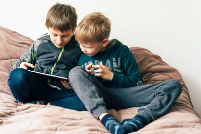 Rear view of siblings sitting on bed