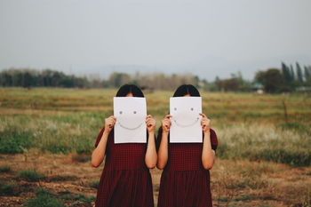 Girls holding smiley face drawn papers in front of face on field