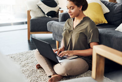 Young woman using mobile phone while sitting on sofa at home