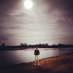 Rear view of man standing by lake against sky